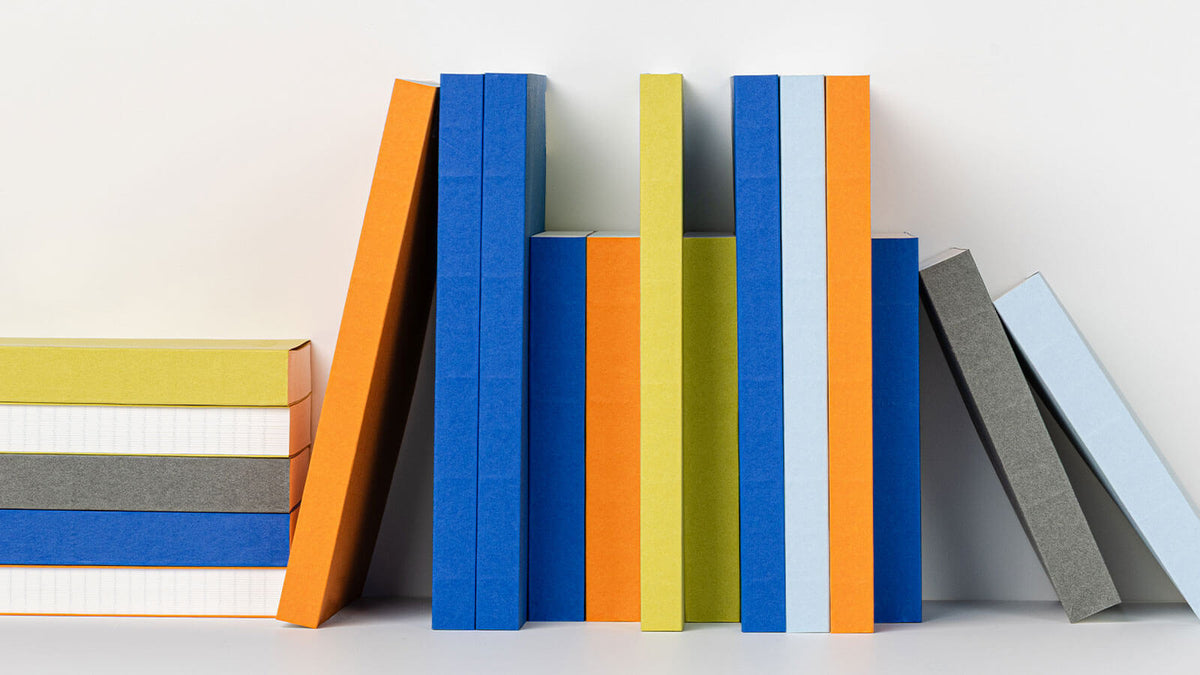 Rij Naked-notitieboeken van mishmash in blauw, oranje, geel, lichtblauw en grijs op een witte plank
