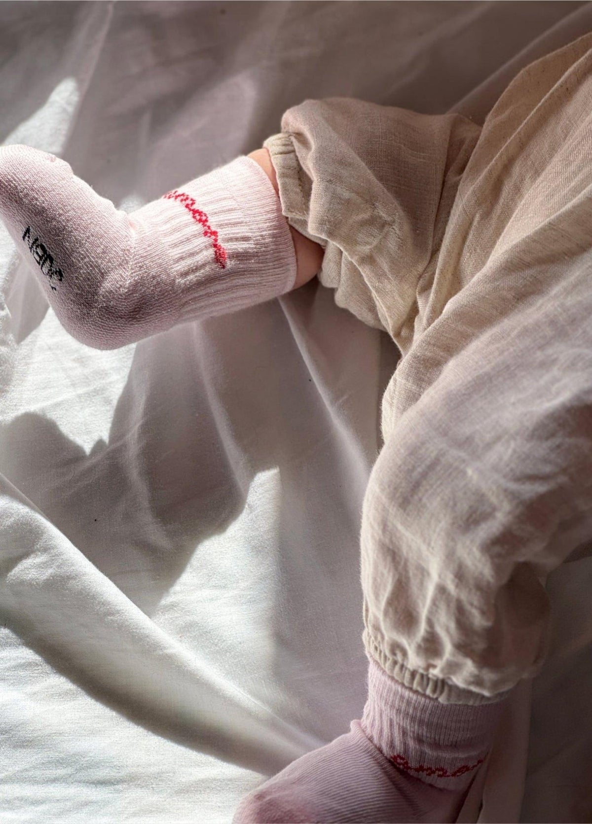 Babyvoetjes in lichtroze babysokken Amore van No Bad Days Club met rood opschrift