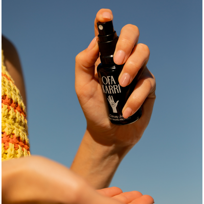 Hand houdt de Citrusy Joy handspray van Ofa Karri omhoog tegen een blauwe lucht