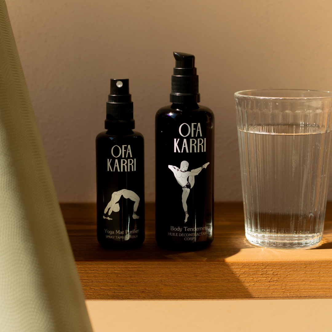 Body Tenderness massageolie en Yoga Mat Purifier van Ofa Karri op een houten tafel naast een glas water
