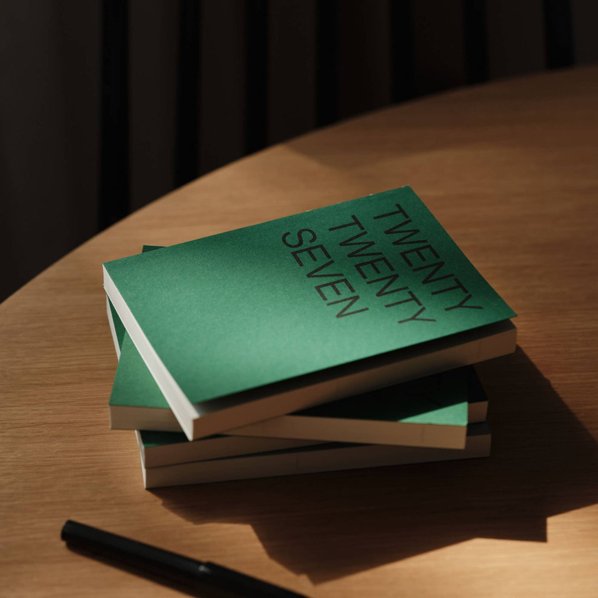 Gestapelde agenda's 2027 Emerald van This Might Work op een ronde houten tafel met een pen