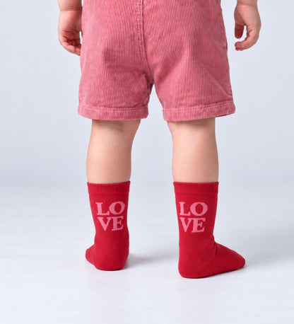 Peuter met rode babysokken Love van No Bad Days Club met roze opschrift 'LOVE'