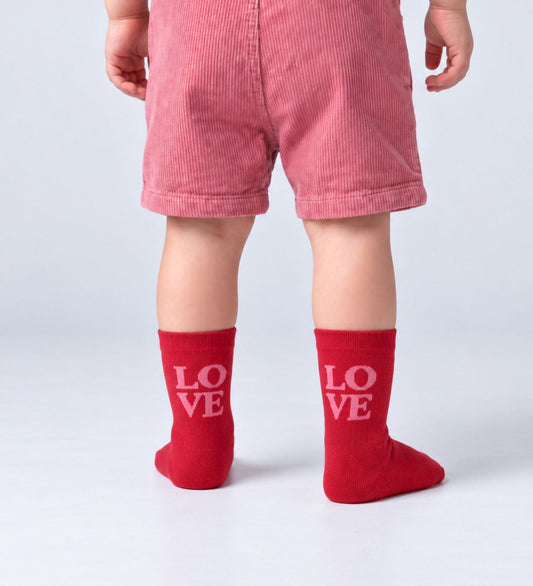 Peuter met rode babysokken Love van No Bad Days Club met roze opschrift 'LOVE'