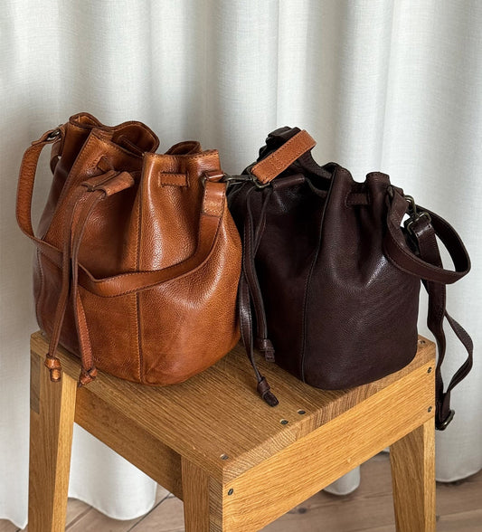 Bucket bags Olive van Montana Est. 1957 in cognac en bruin op een houten krukje